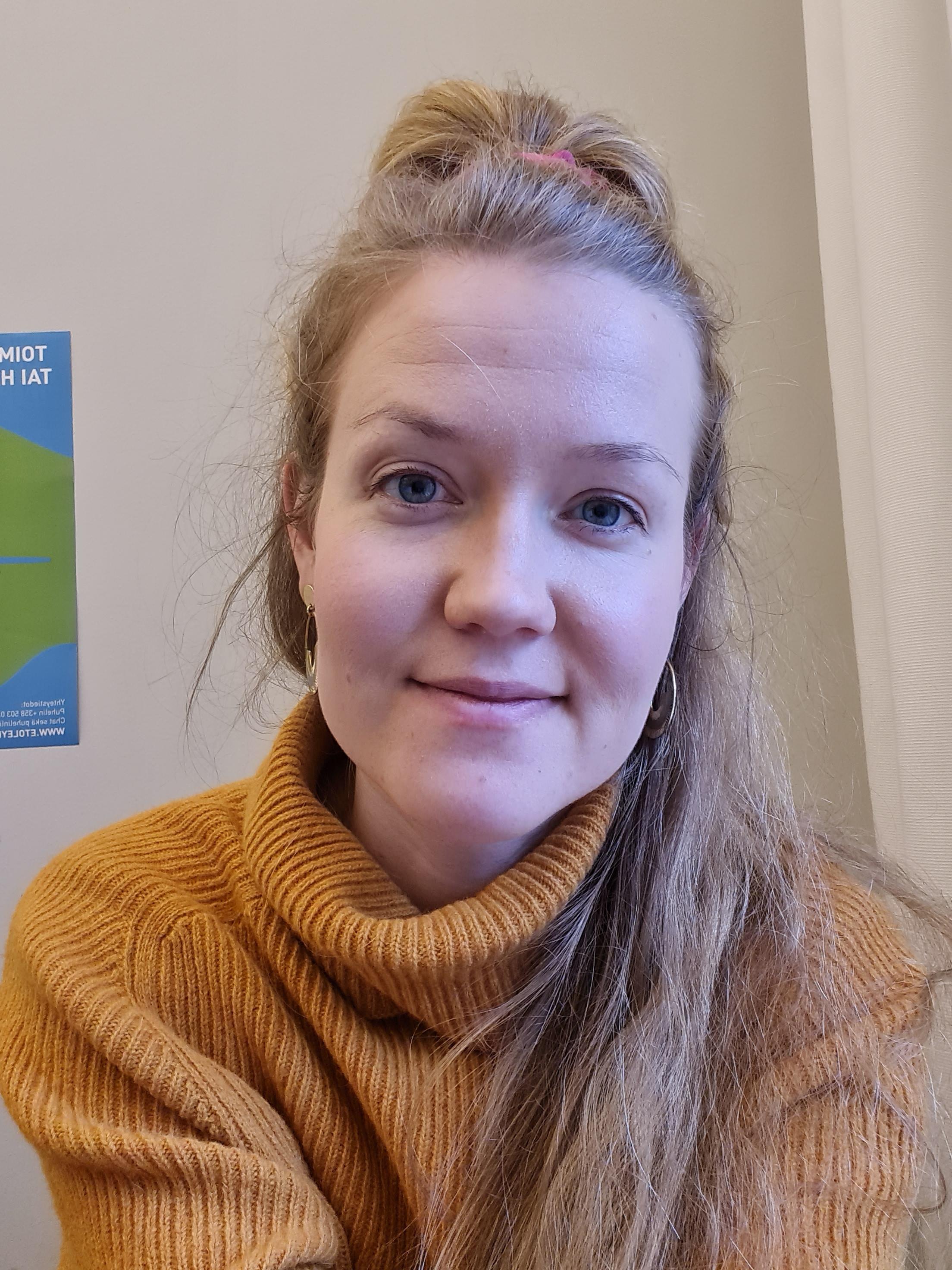 Viivillä on keltainen korkeakauluksinen villapaita sekä vaaleahkot pitkät hiukset ja vaalea iho.