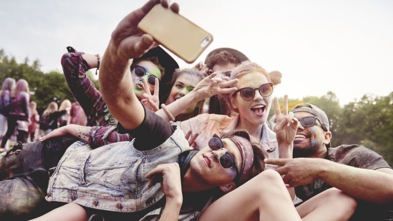 Iso joukkoa nuoria makaa ulkona maassa, auronkolasit päässä ja ottavat selfietä.