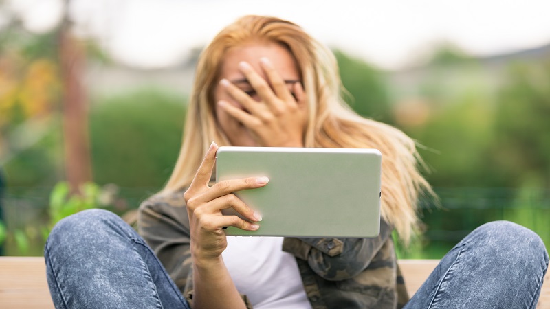 girl wathing tablet and holding her hand in her face with embarrasement