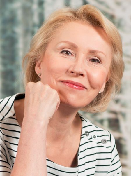 Raisa Cacciatoren kuva, jossa nojaa käteen ja hymyilee, päällä raidallinen paita.