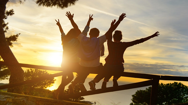 young people holding their hands up and wathcing sunset in a fence