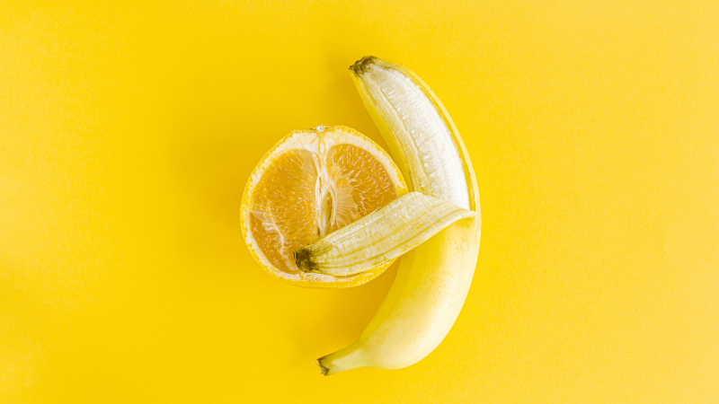Puolikas appelsiini ja osin kuorittu banaani vierekkäin.
