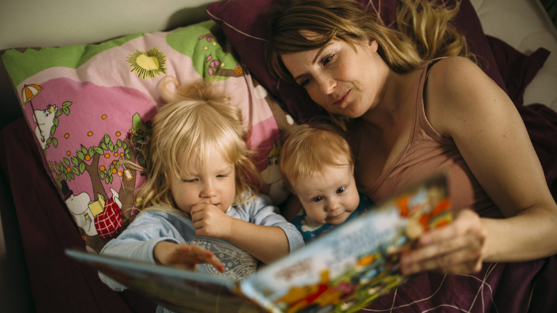 Äiti lukee kirjaa kahdelle pienelle lapselle.