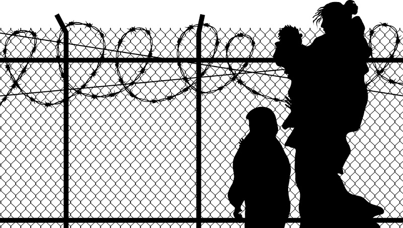 silhouette of refugee woman with two children. in front of spike fence