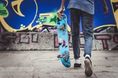 Pojke, fotograferad bakifrån, med en skateboard i vänstra handen, går mot skaterampen.