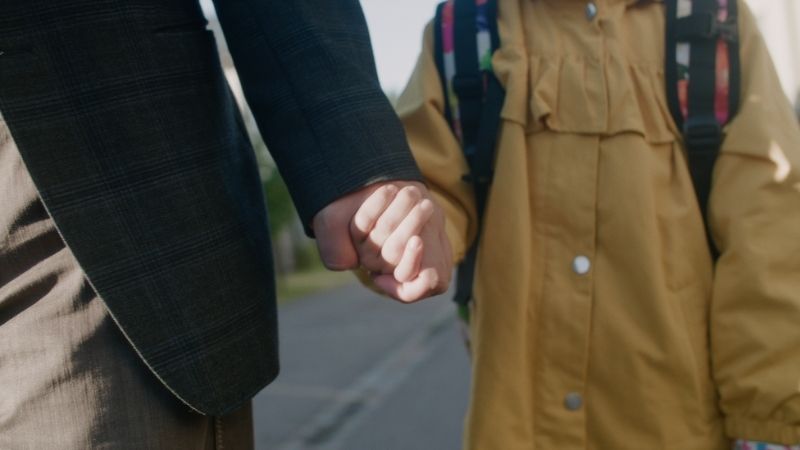 A parent and a child holding hands and wearing autumn clothes.