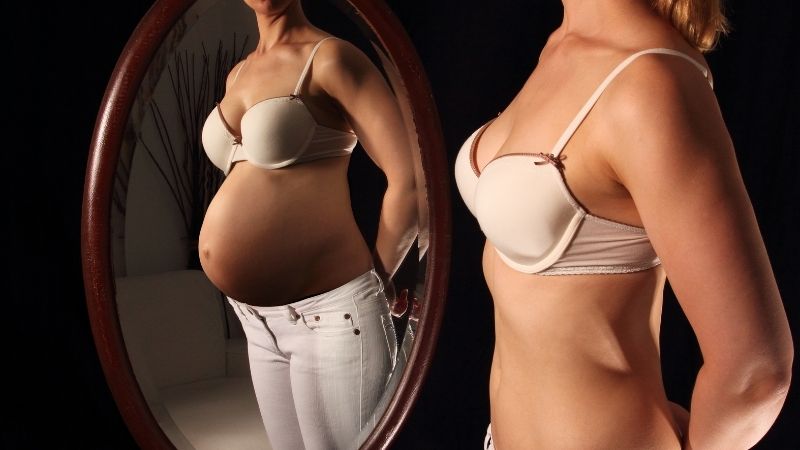 Hoikka nainen katsoo itseään peilistä ja näkee itsensä raskaana.
