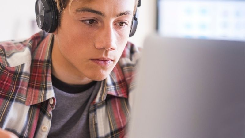 Nuori poika kuulokkeet korvillaan katselee keskittyneesti tietokonetta.