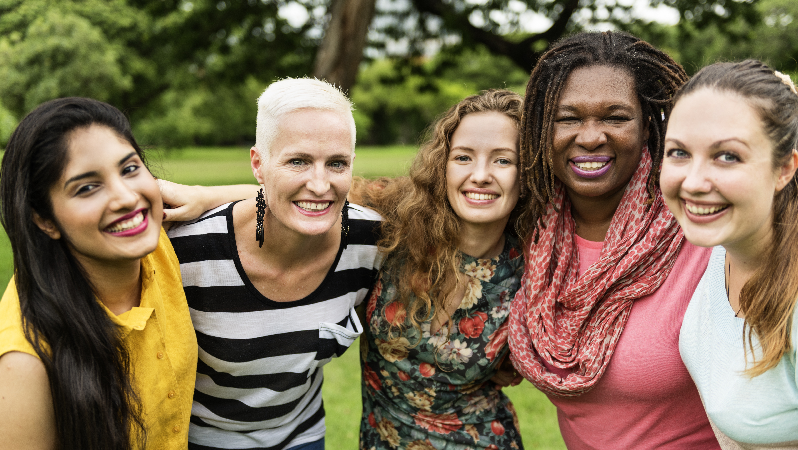 Viisi naista hymyilee puistossa