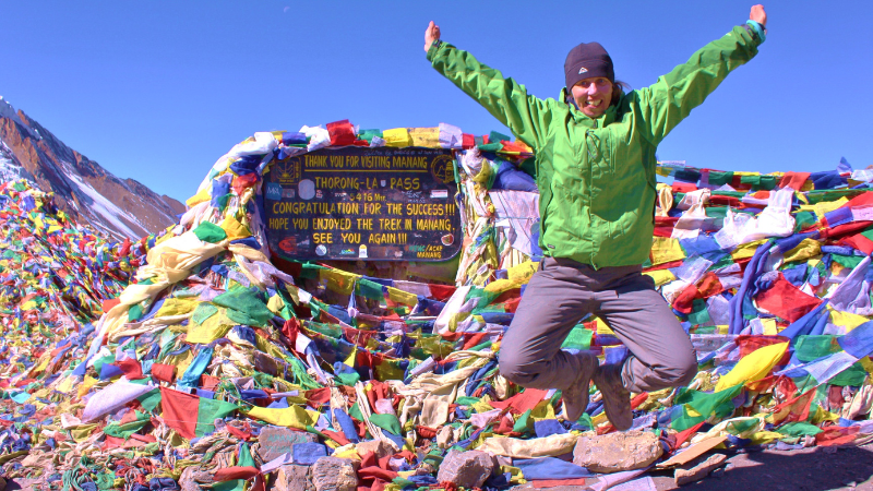 Kuvassa henkilö Nepalissa vuoren huipulla, hyppää kädet auki ilmaan.