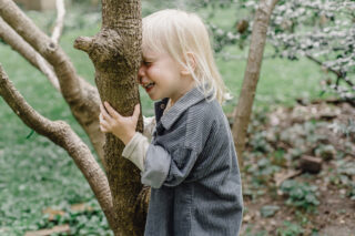 Tarina 6 Pikkulapsi pitää puunrungosta kiinni ja painaa päänsä nauraen sitä vasten. Hän pitää silmiään kiinni.