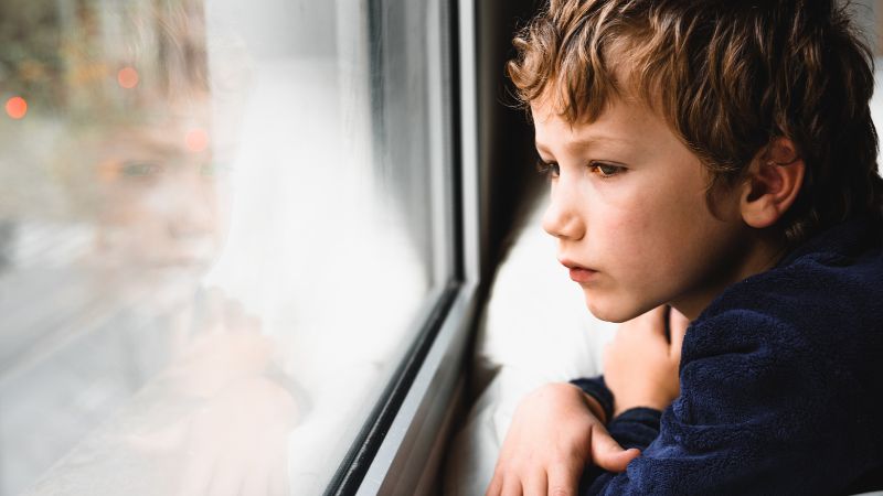 Pieni surullinen poika katselee ikkunasta ulos.